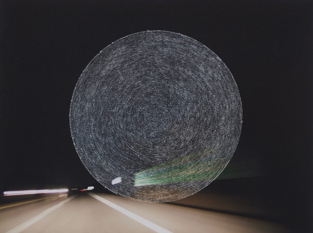 Photograph of a highway at night that has concentric circles scratched into the center of the image.