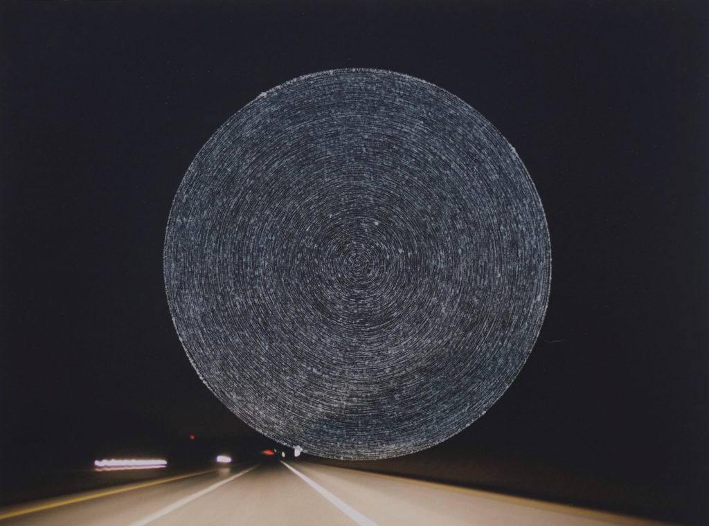  Photograph of a highway at night that has concentric circles scratched into the center of the image.