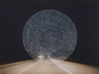 Photograph of a highway at night that has concentric circles scratched into the center of the image.