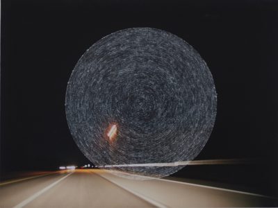 Photograph of a highway at night that has concentric circles scratched into the center of the image.