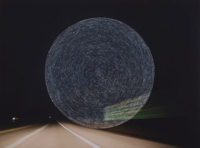 Photograph of a highway at night that has concentric circles scratched into the center of the image.