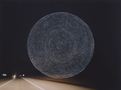 Photograph of a highway at night that has concentric circles scratched into the center of the image.